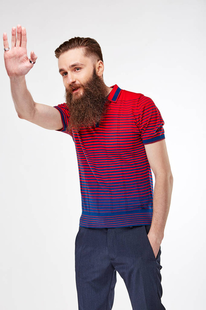 Young bearded man posing in studio in trendy red and blue t shirt with stripes and blue chinos - Fotoğraf, Görsel