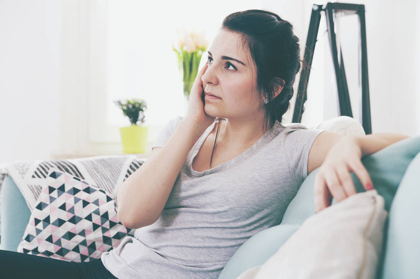 Young worried woman with headache while sitting on comfortable sofa - Foto, Imagem