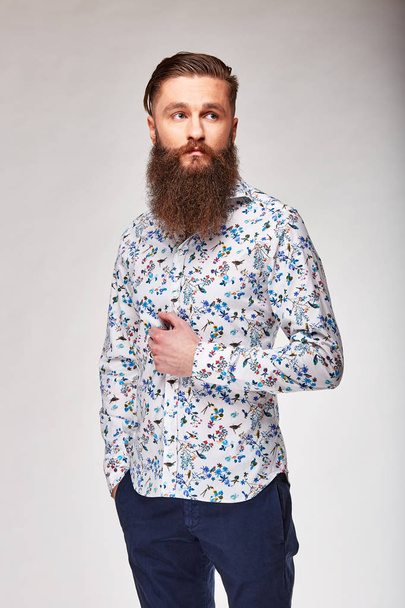 Young bearded man posing in studio in cute white shirt with blue flowers and blue pants - Foto, Imagem