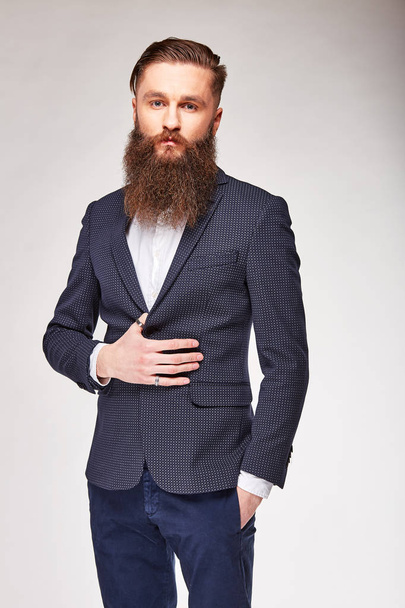 Young bearded man posing in studio in grey trendy blazer, white shirt and blue pants - Photo, Image