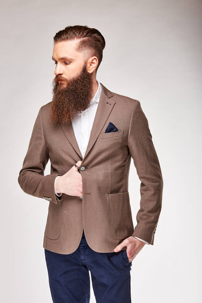 Young bearded man posing in studio in light brown trendy blazer, white shirt and blue pants - Foto, Bild