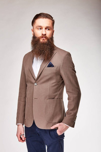 Young bearded man posing in studio in light brown trendy blazer, white shirt and blue pants - Fotografie, Obrázek
