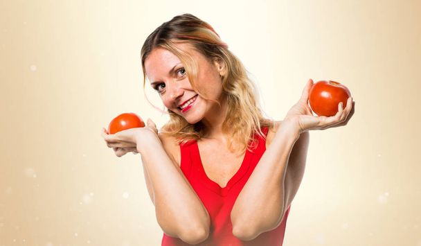 Mooie blonde vrouw met tomaten op okergeel achtergrond - Foto, afbeelding