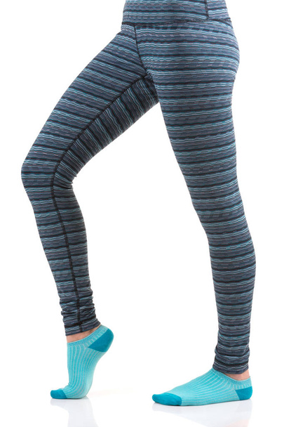 Κλείνω πάνω θέα του γυναίκα πόδια σε πολύχρωμα ριγέ παντελόνι θερμική και μπλε κάλτσες από την πλαϊνή όψη στέκεται στο ένα πόδι με άλλα κλίση στο γόνατο πόδι - Φωτογραφία, εικόνα