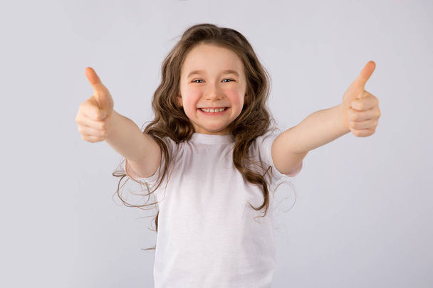 Malá dívka ukazuje palec nahoru gesto v bílé tričko izolovaných na bílém pozadí. - Fotografie, Obrázek