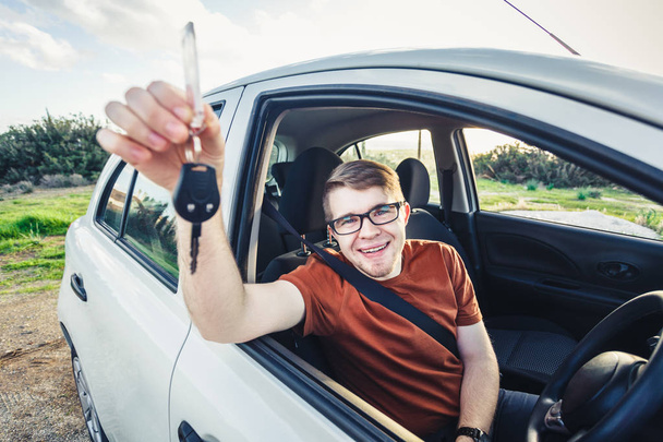 Houkutteleva nuori mies näyttää uusia auton avaimia ja hymyilee
 - Valokuva, kuva