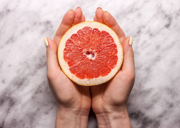 female hands keeping cut grapefruit - Foto, afbeelding