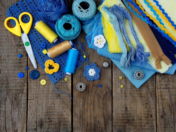 gele en blauwe accessoires voor handwerk op bruin houten achtergrond. Breien, borduren, naaien. Kleine bedrijven. Inkomsten uit hobby. - Foto, afbeelding