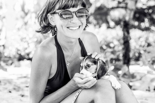Menina atraente nova com seu cão de estimação Beagle na praia da ilha tropical Bali, Indonésia. Momentos felizes. Foto em preto e branco
. - Foto, Imagem