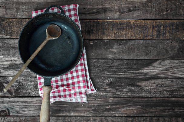 Black frying pan with a wooden spoon on a brown wooden surface - Photo, image