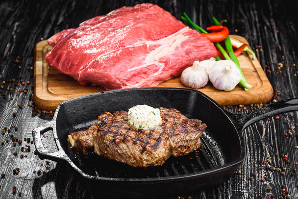 gegrilltes schwarzes Angus-Steak auf Grilleisen-Pfanne auf schwarzem Holzhintergrund mit rohem  - Foto, Bild