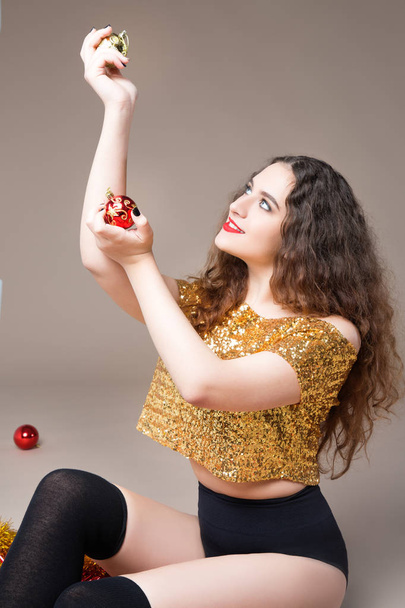 Young beautiful girl in a gold dress with Christmas balls and red Christmas toys - 写真・画像