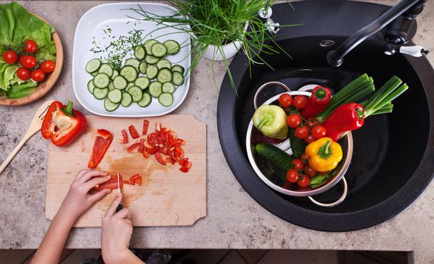 Mãos de criança que cortam verduras de uma salada - visão superior
 - Foto, Imagem
