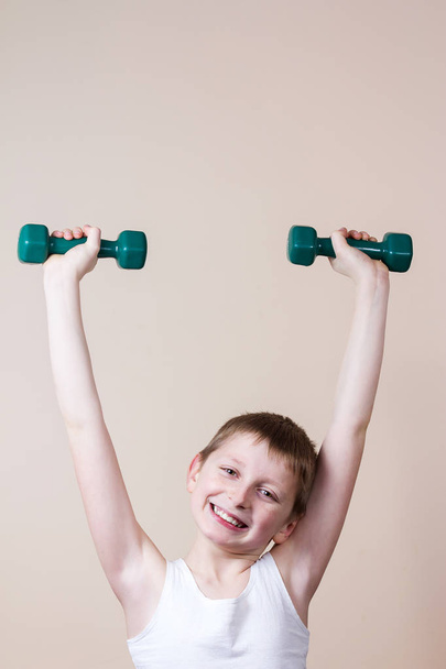 Strong little boy looking at camera  while exercising with dumbb - Foto, imagen