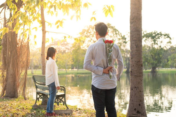 zadní pohled mladý muž právě dává kytice červená květina pro přítelkyni - Fotografie, Obrázek