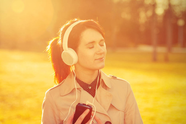 Woman listening to music in headphones in park  in sunlight in a sunny day - Фото, изображение