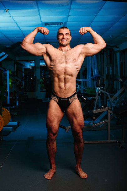 bel homme avec de gros muscles, posant à la caméra dans la salle de gym - Photo, image