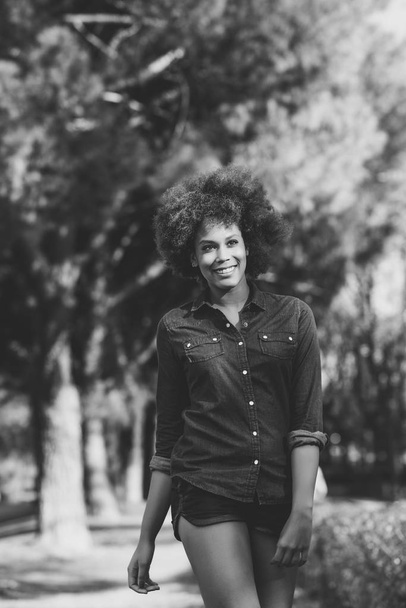 Joven mujer negra con peinado afro caminando en parque urbano
 - Foto, imagen