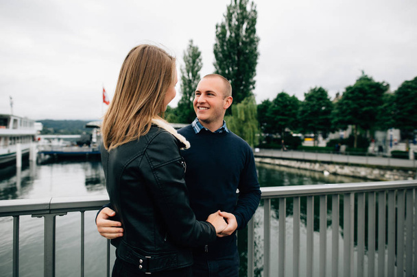 Young couple in love standing on bridge looking at each other and smiling - Photo, Image