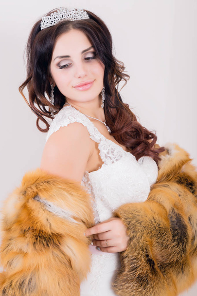 Beautiful young bride wearing white wedding dress and fur coat with professional make-up - Fotoğraf, Görsel