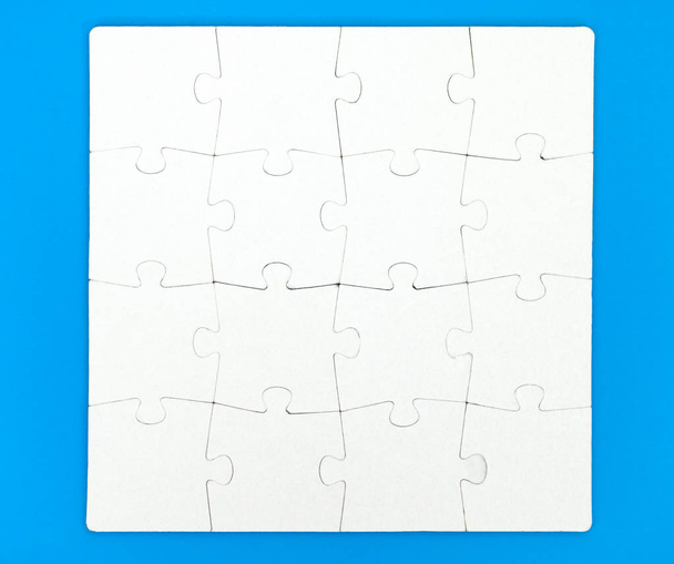 White puzzle with sixteen pieces on blue background - Fotó, kép