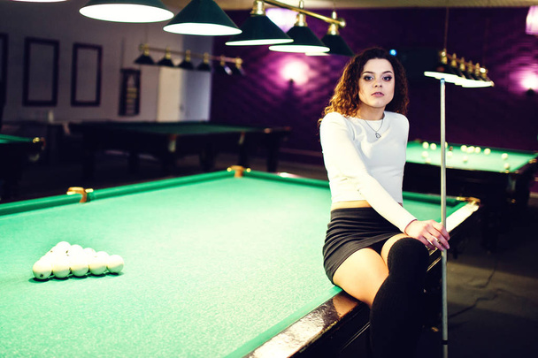 Young curly girl posed near billiard table. Sexy model at black  - Foto, imagen