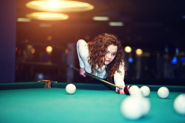 Young curly girl posed near billiard table. Sexy model at black  - Фото, изображение