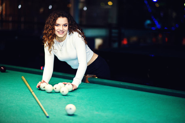 Young curly girl posed near billiard table. Sexy model at black  - Фото, зображення