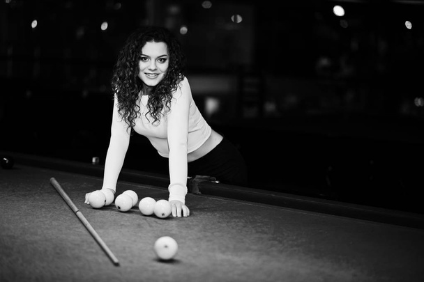 Young curly girl posed near billiard table. Sexy model at black  - Фото, зображення