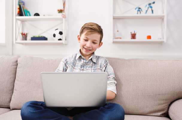 Хлопчик-підліток використовує ноутбук на дивані вдома
 - Фото, зображення