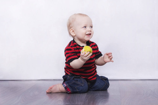 Очаровательный младенец сидит на сером полу с яблоком
 - Фото, изображение