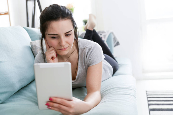Young woman using pc tablet while lying on comfortable sofa - Fotoğraf, Görsel