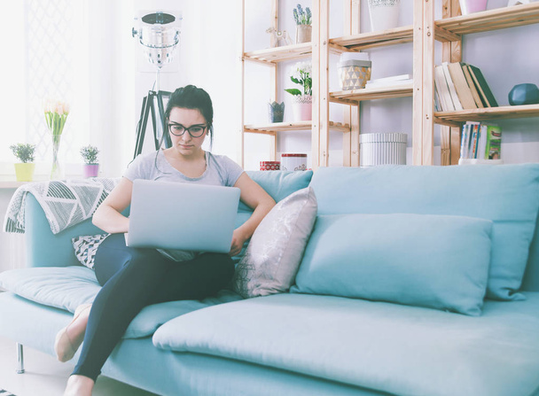 Young woman using laptop while sitting on comfortable sofa, home - Foto, afbeelding