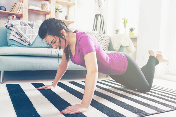 Young woman exercising on carpet at home interior - Foto, afbeelding