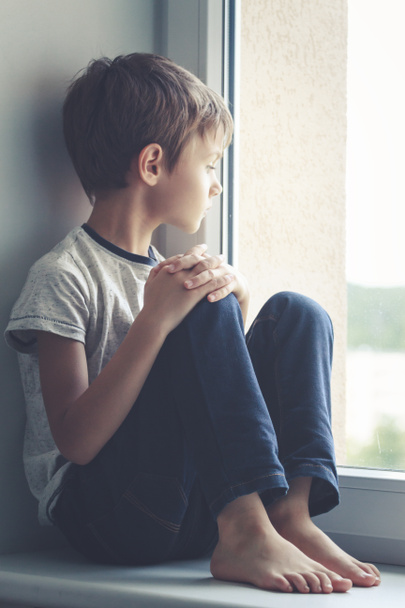 Surullinen lapsi istuu ikkunassa kilpi ja katselee ulos ikkunasta
 - Valokuva, kuva
