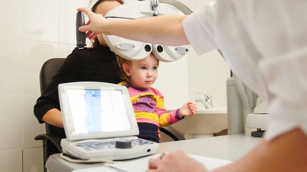 Оптометрист в клинике проверяет зрение маленьких девочек - детская офтальмология
 - Фото, изображение