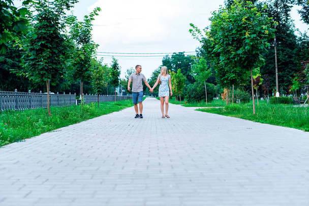 Young modern couple is walking in the park holding hands, in summer in the city, horizontal in full growth, family on nature is resting, the concept of a happy family. - Foto, imagen