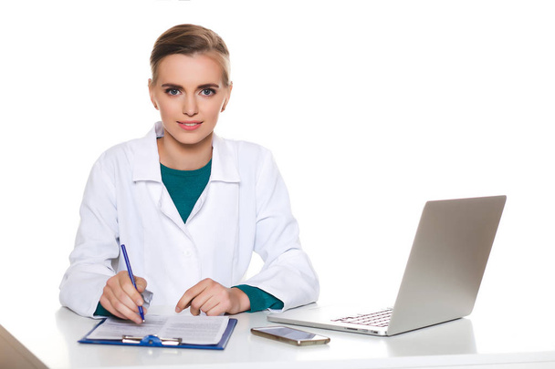 Jonge vrouwelijke student arts zitten met een laptop op een witte achtergrond - Foto, afbeelding