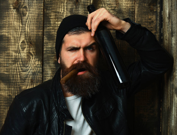 Bearded brutal caucasian hipster holding bottle and smoking cigar - Фото, изображение