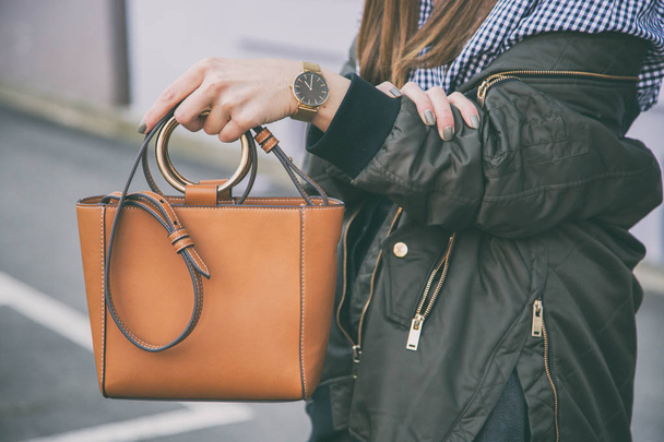 κοντινό πλάνο λεπτομέρειες της μόδας, κρατώντας καφέ κομψή τσάντα της γυναίκας. φορώντας μαύρο και χρυσό ρολόι. ιδανικό ελατήριο στολή accessories.fashion blogger που θέτουν σε μια κορυφή gingham check και ένα σακάκι βομβαρδιστικό. - Φωτογραφία, εικόνα