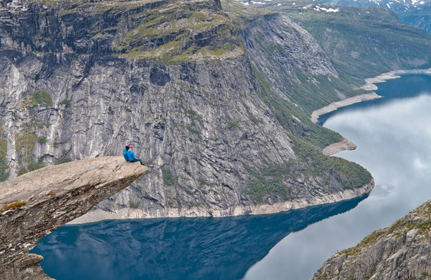 Pessoas sentadas na rocha Trolltunga (Rocha da Língua do Troll) e olhando para a paisagem montanhosa norueguesa
 - Foto, Imagem