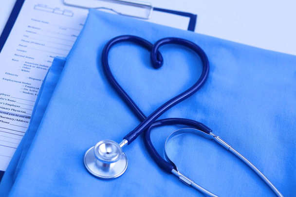 Zdravotní stetoskop stočeny do tvaru srdce leží na seznamu pacienta anamnézu a modré doktor jednotné closeup. Lékařskou pomoc nebo pojištění konceptu. Kardiologická péče, zdraví, ochrana a prevence - Fotografie, Obrázek