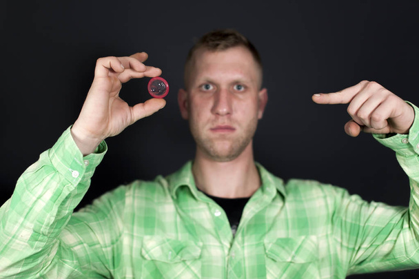  Adam göstermek için koyu renk arka plan önünde kırmızı prezervatif parmağında.  - Fotoğraf, Görsel