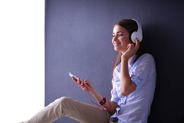 Smiling girl with headphones sitting on the floor near wall - 写真・画像