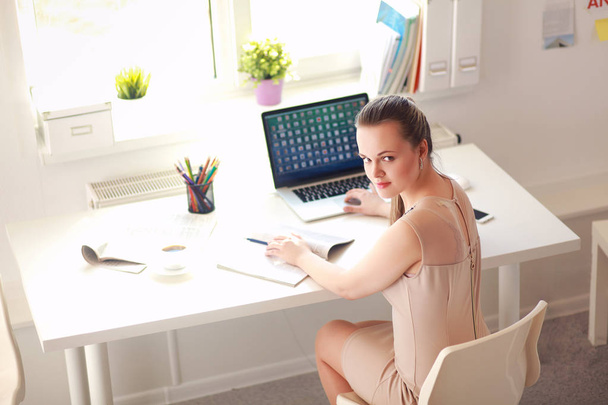 Γυναίκα με έγγραφα που κάθονται στο γραφείο και το φορητό υπολογιστή - Φωτογραφία, εικόνα
