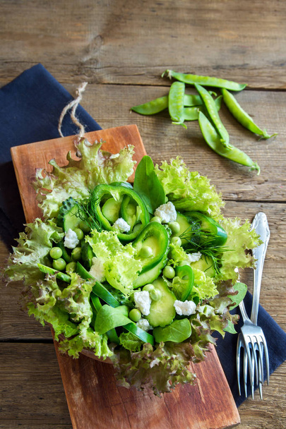 Organic mixed green vegetable salad with feta cheese in wooden bowl close up - healthy diet organic vegan vegetarian food meal salad - Fotó, kép
