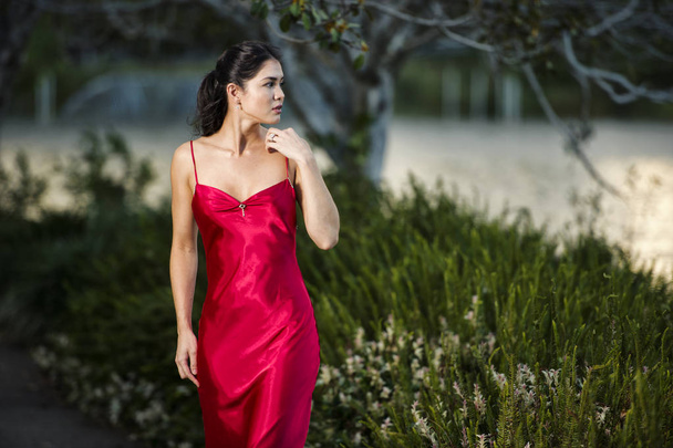 Piękna młoda kobieta w ogrodach noszenie długich jedwabnych dre czerwony - Zdjęcie, obraz
