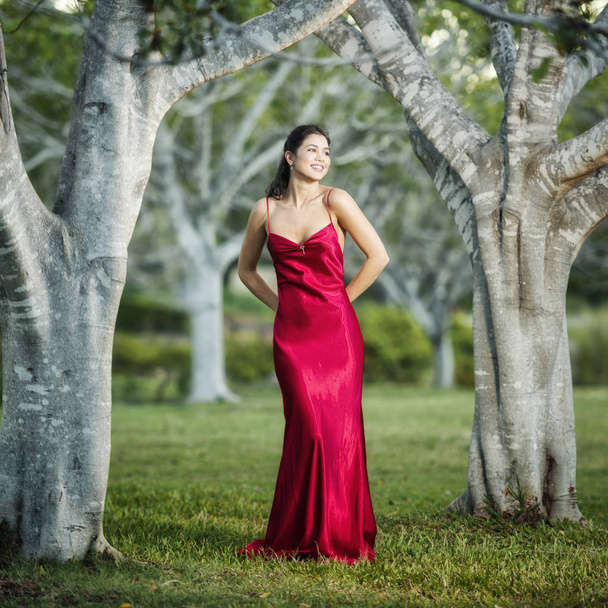 A kertben egy hosszú selyem piros ruha visel a gyönyörű fiatal nő - Fotó, kép