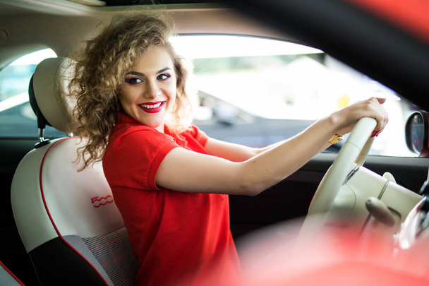 Ездил по городу. Молодая привлекательная женщина улыбается и смотрит прямо во время вождения автомобиля
 - Фото, изображение