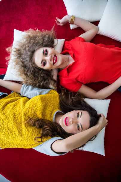 Vista dall'alto di due amiche sorridenti donne sdraiate sul divano con sorriso
 - Foto, immagini